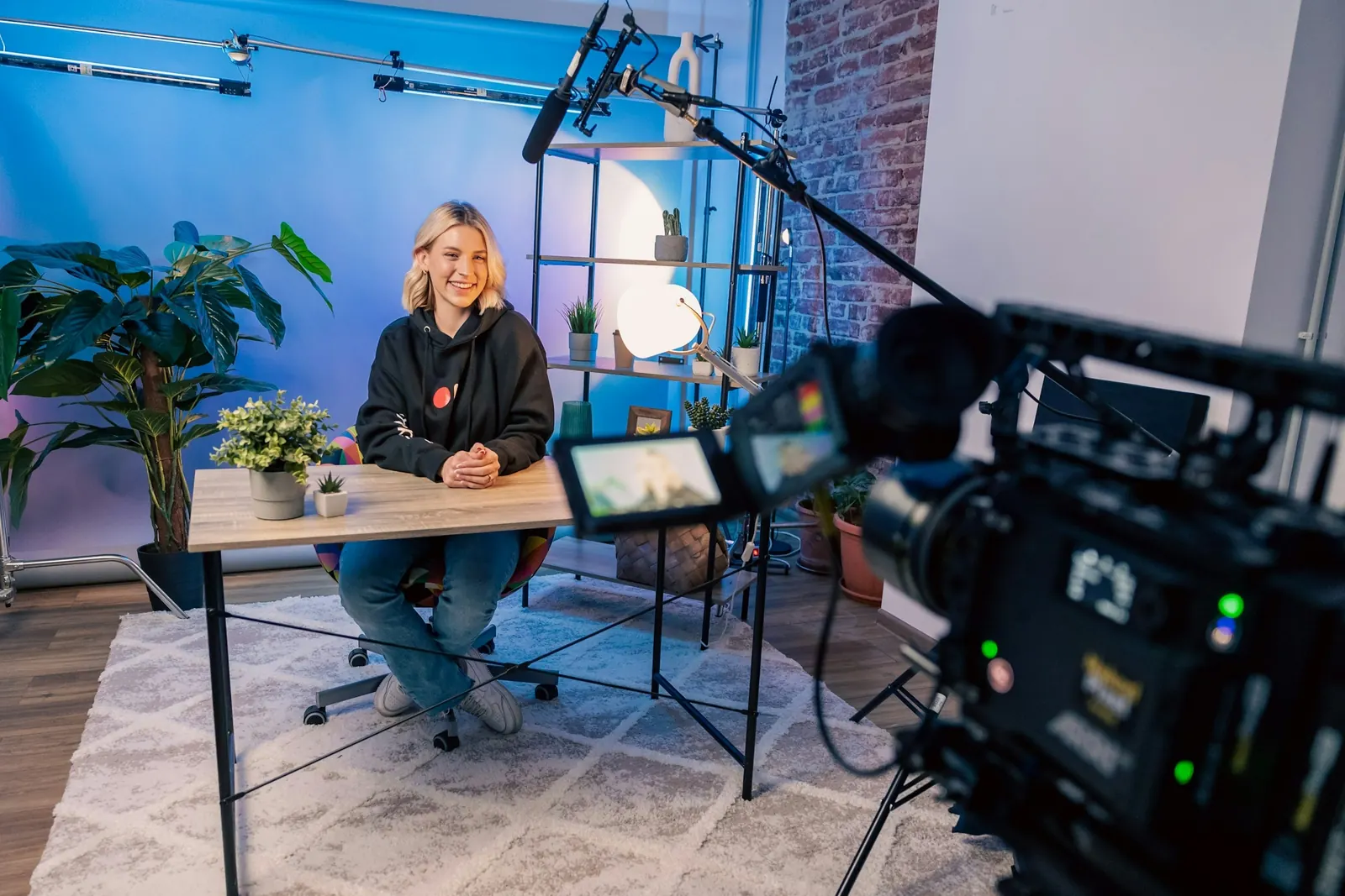 A presenter seated at a desk in a studio, filmed by a video camera