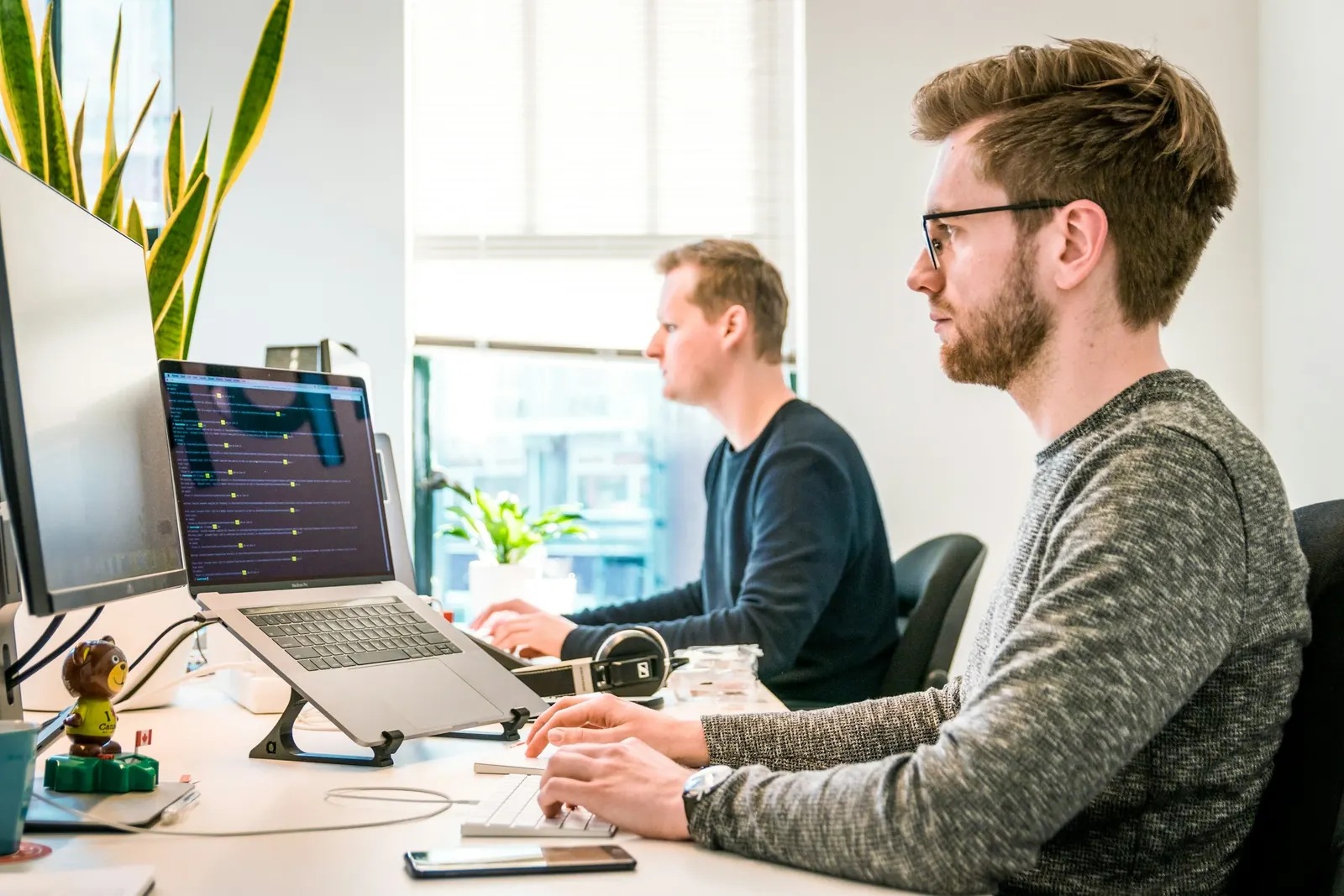 Two developers writing code at their desks in a bright office