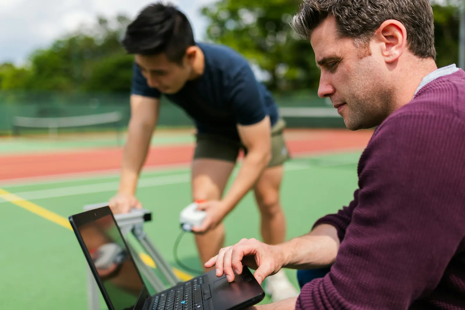 A coach reviewing training data on a laptop courtside