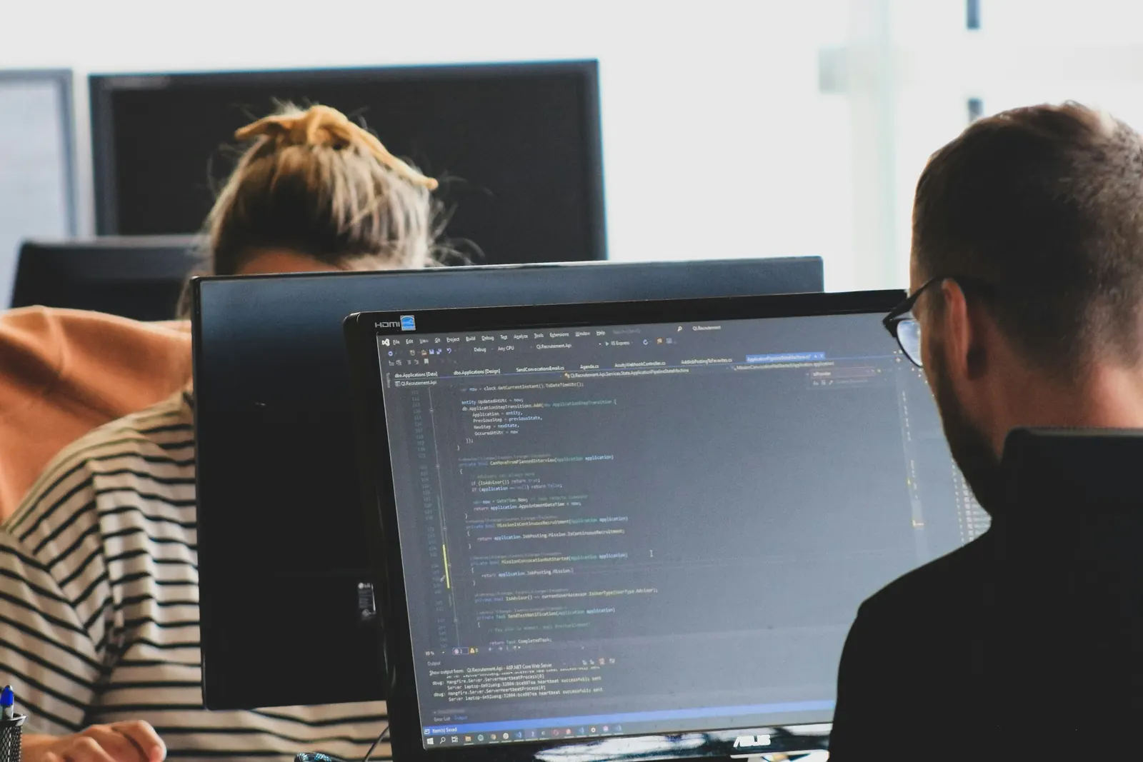 Two people writing code at desktop monitors in an office
